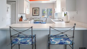 Una cocina moderna con una isla central, dos taburetes de bar y un techo de color naranja brillante.