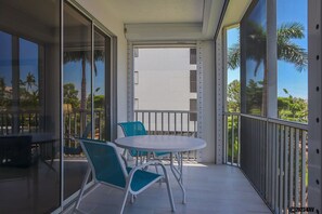 Een balkon met een ronde tafel en twee stoelen, met uitzicht op een woongebied met palmbomen en een heldere lucht.