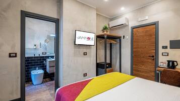 Camera d'albergo moderna con un letto, bagno con lavandino e specchio, armadio e televisore che mostra il nome dell'hotel.
