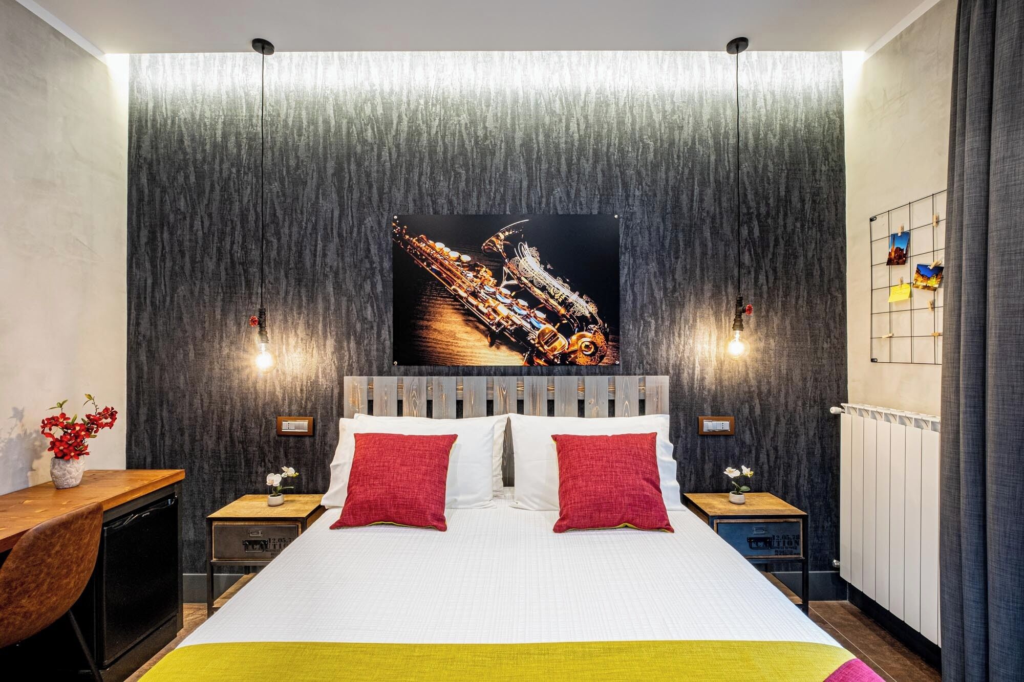 Habitació d'hotel moderna amb un llit gran, dues taules de nit, un escriptori de fusta i una obra d'art penjada a la paret.