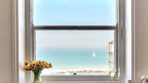 A window with a view of the sea and a sailboat, a vase with flowers, and a glass of water on the windowsill. - The Lookout Broadstairs, 3 bed 2 bath Apt, central, sea views, kids & dogs ok (Broadstairs)