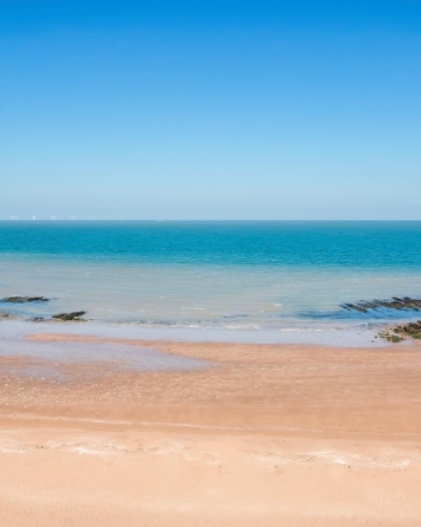 Une plage à l’eau d’un bleu limpide et au rivage sablonneux.