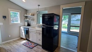 Une cuisine avec un réfrigérateur noir, un plancher en bois, une fenêtre et une vue sur un lac.
