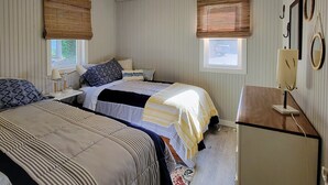Une chambre avec deux lits, un ventilateur de plafond, un bureau et une fenêtre avec des stores.