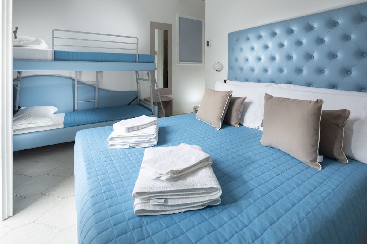 A hotel room with a bunk bed, a large bed with blue bedding, and a tufted headboard.