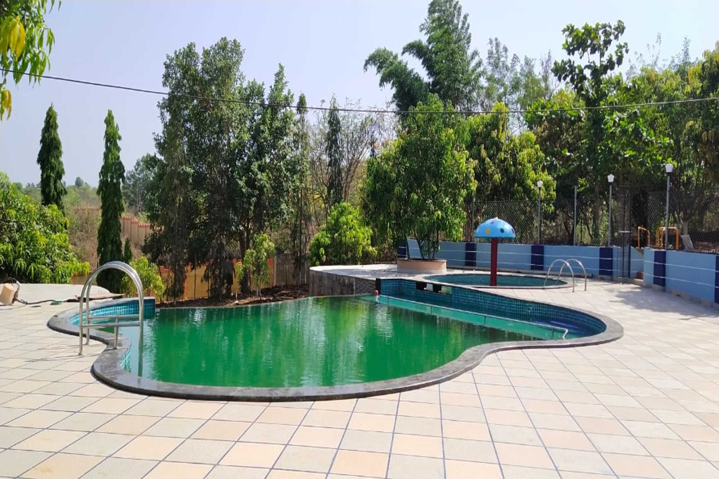 A swimming pool with a tiled deck, surrounded by trees and a fence.