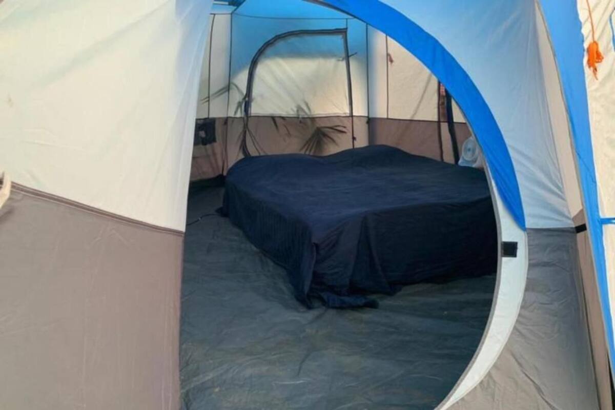 Une tente avec un lit à l’intérieur, une porte visible et une vue partielle sur une fenêtre.