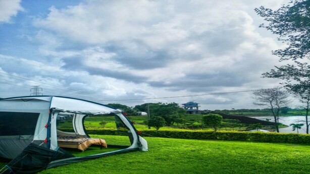 A tent set up on a grassy area with a view of a lake and trees in the background. - Campistaan Badlapur (Ambernath)