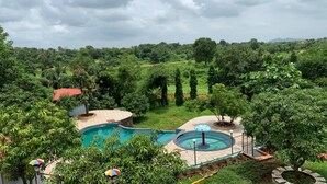 A swimming pool surrounded by lush greenery and trees, with a cloudy sky above. - Campistaan Badlapur (Ambernath)