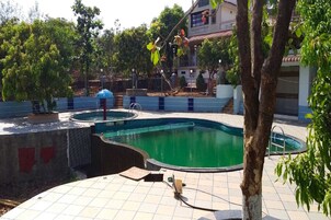 A swimming pool area with a tiled deck, a small circular pool, and a tree in the foreground.