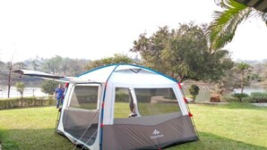 A camping tent with a mesh door and a rainfly, set up on a grassy area near a body of water. - Campistaan Badlapur (Ambernath)
