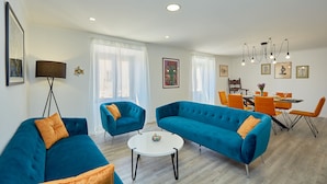 Un salon moderne avec des canapés bleus, une table basse blanche et un coin repas avec des chaises orange et une table blanche.