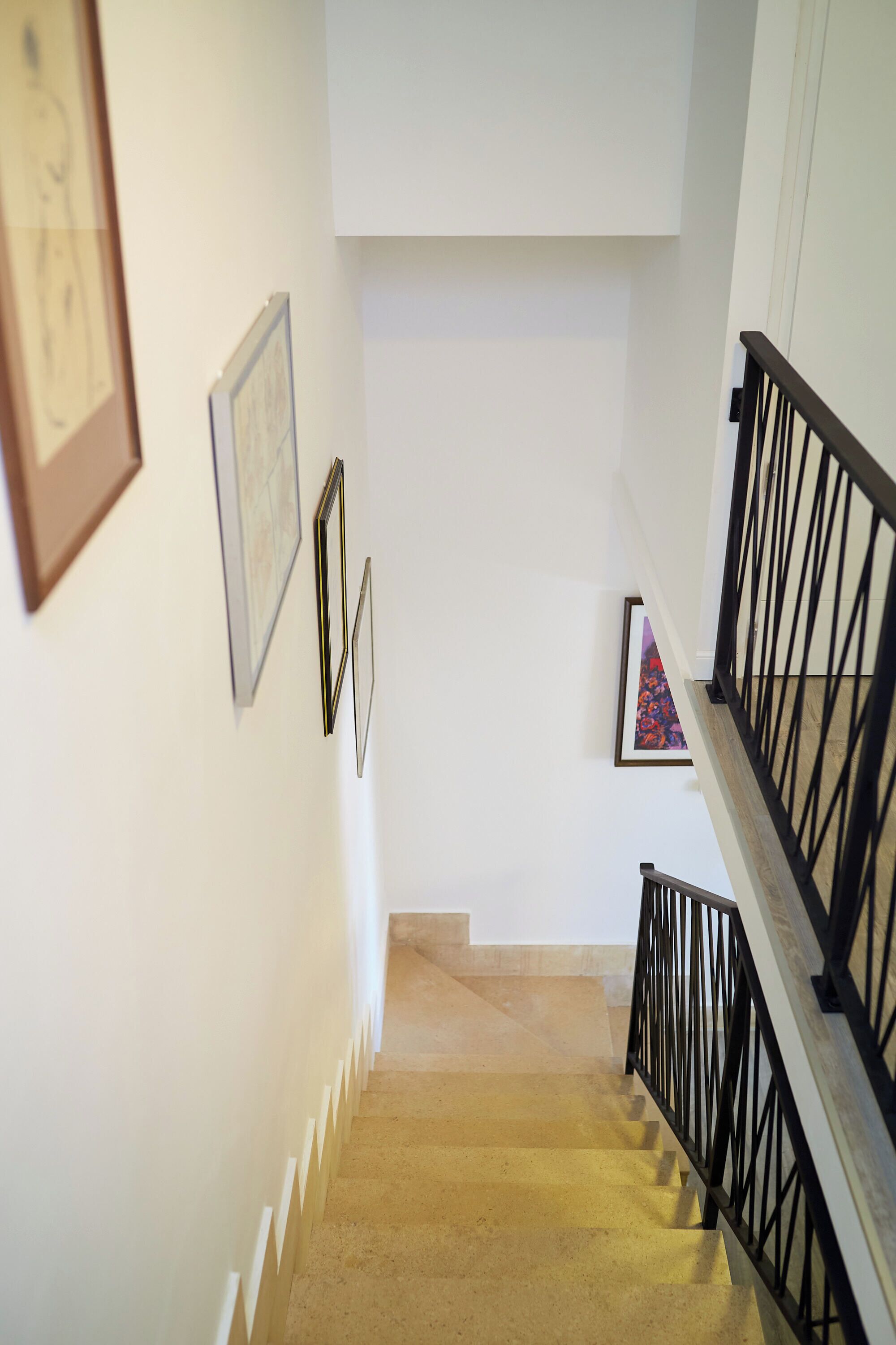 A staircase with a black railing, white walls, and framed artwork.