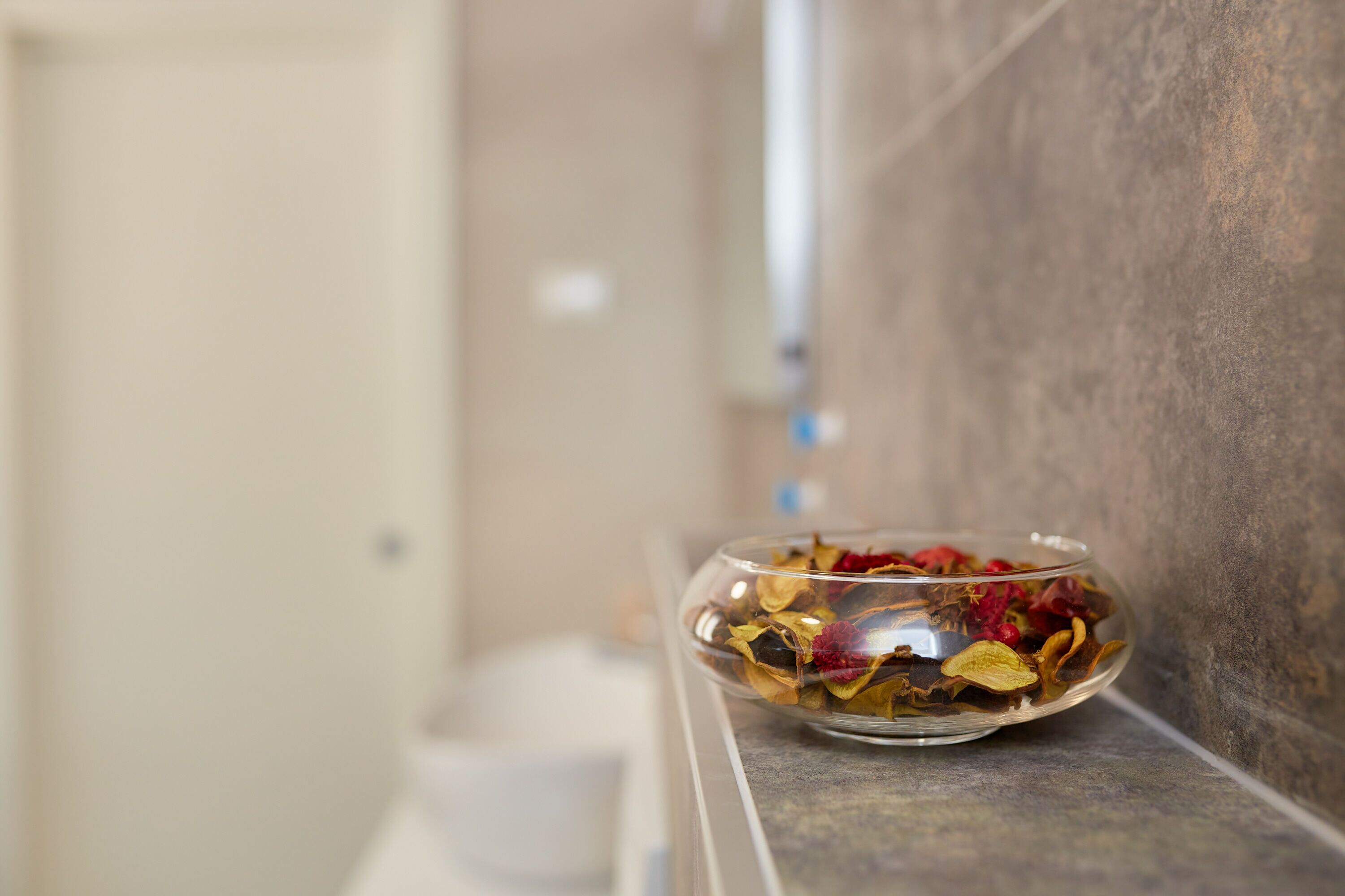 A clear glass bowl filled with dried flowers and leaves on a marble ledge.
