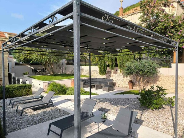 A covered outdoor seating area with metal furniture and a stone wall backdrop.