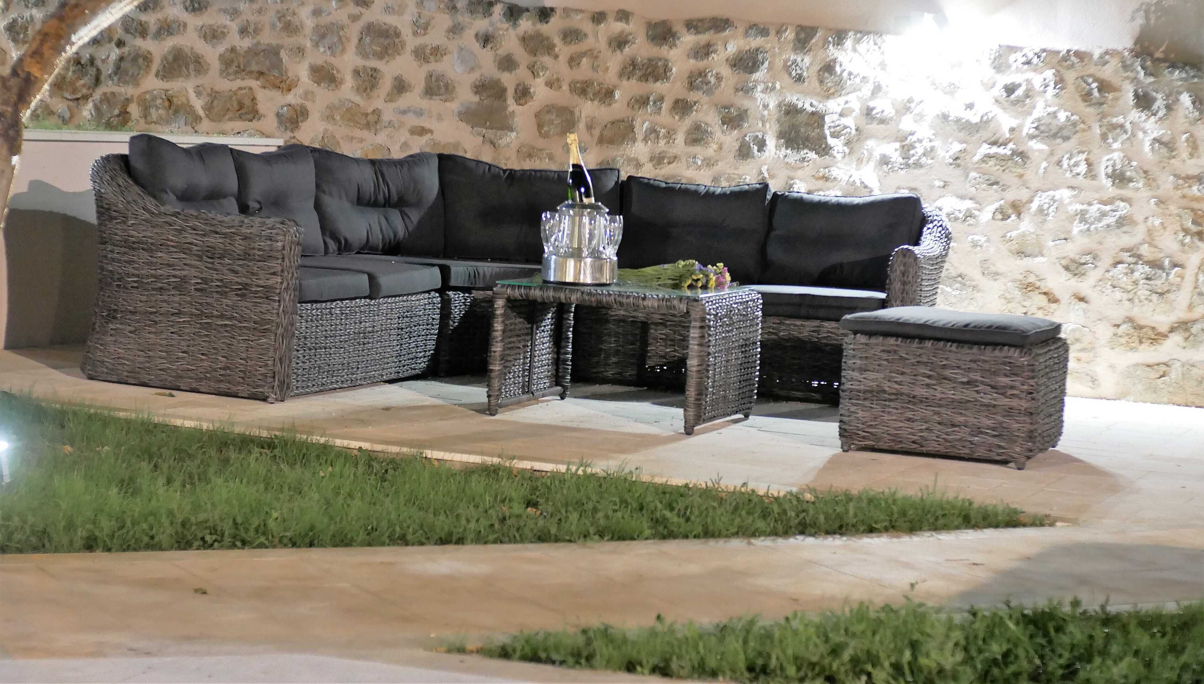A wicker sofa set with a glass table and a bottle of champagne, set against a stone wall.