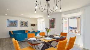 Un coin repas avec une table dressée pour quatre personnes, entouré de chaises orange, d’un canapé bleu et d’un lustre.