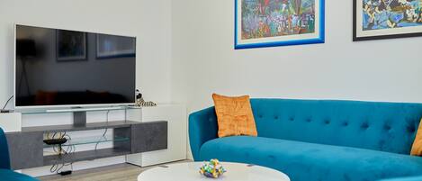 A modern living room with a flat-screen TV, a blue sofa, and two framed artworks on the wall.