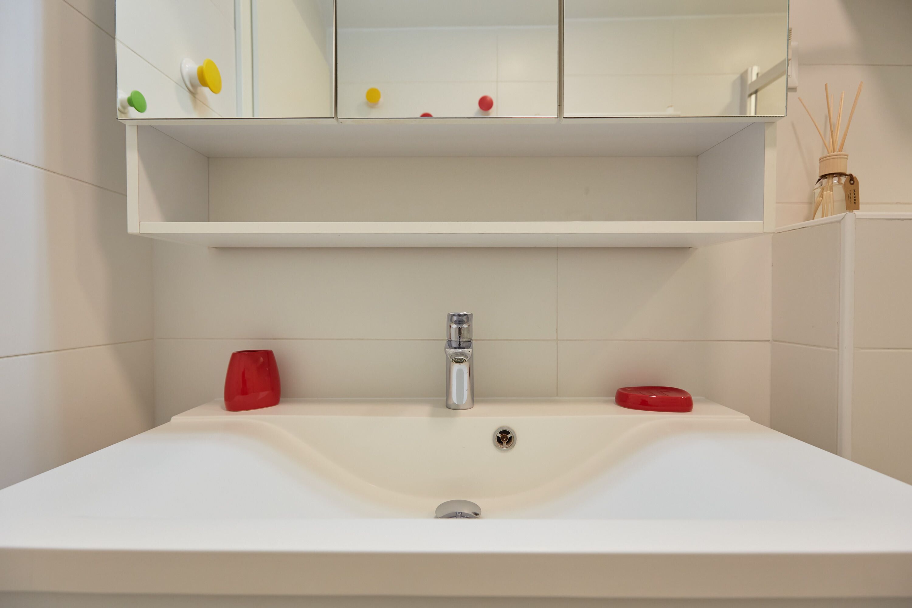 A bathroom with a white sink, a mirror above it, and a shelf with a few items.