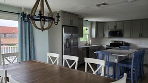 A modern kitchen with a central island, stainless steel appliances, and a dining area with white chairs. - Newly renovated! 5 bedroom 2 bath home woth AC and walk to water (Narragansett)