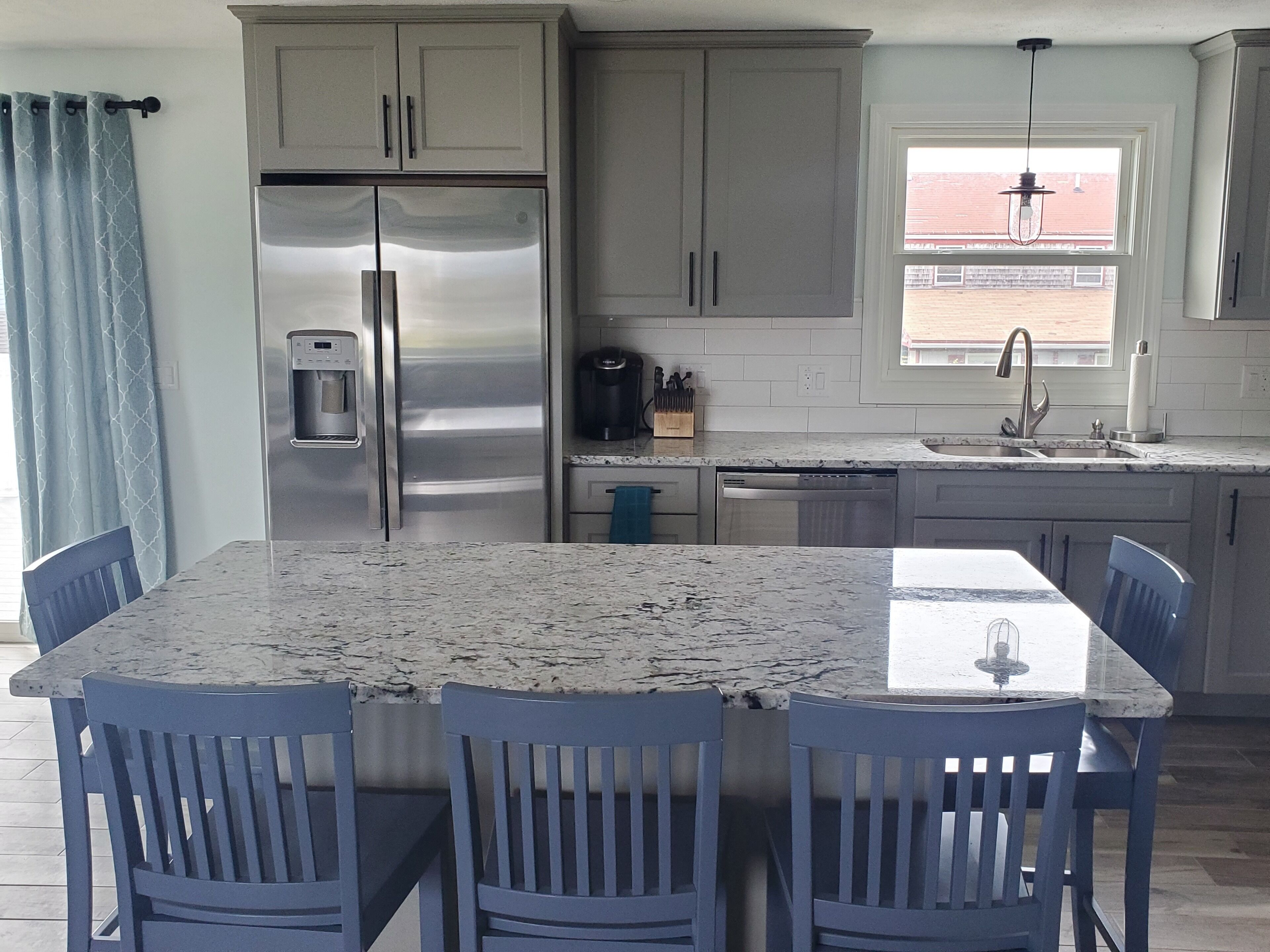 A kitchen with a stainless steel refrigerator, a coffee maker, and a sink. There are four blue chairs around a marble table.