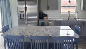 A kitchen with a stainless steel refrigerator, a coffee maker, and a sink. There are four blue chairs around a marble table. - Newly renovated! 5 bedroom 2 bath home woth AC and walk to water (Narragansett)