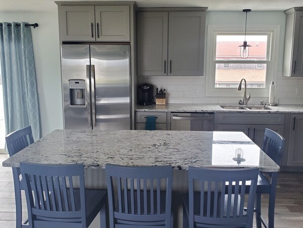 A kitchen with a stainless steel refrigerator, a coffee maker, and a sink. There are four blue chairs around a marble table. - Newly renovated! 5 bedroom 2 bath home woth AC and walk to water (Narragansett)