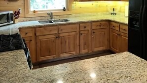 Una cocina con armarios de madera, encimeras de granito, un refrigerador negro y una ventana con vistas a la vegetación.
