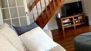 A living room with a wooden staircase, a sofa, a television, and a bookshelf.