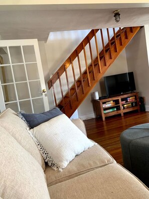 A living room with a wooden staircase, a sofa, a television, and a bookshelf.