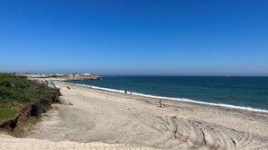 A beach with a clear sky, sandy shore, and a few people walking.