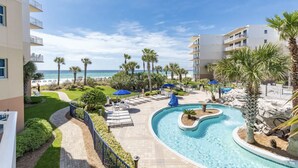 A resort pool area with a curved design, surrounded by palm trees and lounge chairs, overlooking a beach.