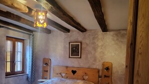 Een slaapkamer met een houten bed, een houten hoofdbord met hartvormige uitsparingen, een nachtkastje, een houten kledingkast en een raam met jaloezieën.
