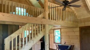 A spacious room with a high ceiling, wooden beams, a staircase, a dining area with a table and chairs, and a ceiling fan. - Persimmon - Hand hewn private log cabin with views (Logan)