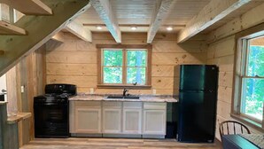 A wooden cabin kitchen with a central island, a stove, and a refrigerator. - Persimmon - Hand hewn private log cabin with views (Logan)