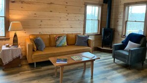 A cozy cabin interior with a wooden floor, a sofa, a chair, a table, and a fireplace. - Persimmon - Hand hewn private log cabin with views (Logan)