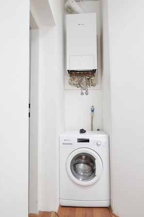 Un espace buanderie compact comprenant un lave-linge à chargement frontal et un radiateur fixé au mur.