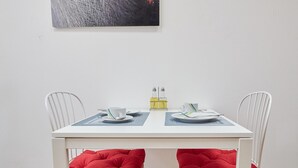 A dining table with two white chairs, each with a red cushion. There are two white plates, two white cups, and a yellow bottle on the table. - Modern Apartment in The Heart of Vienna 1 (Vienna)