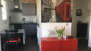 A compact kitchen with grey cabinets, a red cabinet, a dining table with chairs, and a red cabinet with a vase of flowers. - F2 modern and functional with sea view jet countryside Beach juno beach (Courseulles-sur-Mer)