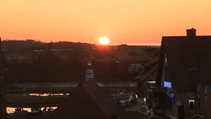 A sunset over a town with buildings and a body of water in the foreground. - F2 modern and functional with sea view jet countryside Beach juno beach (Courseulles-sur-Mer)