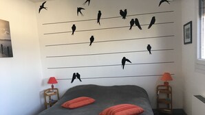 A bedroom with a bed, two red pillows, a nightstand with a red lamp, and a wall decorated with bird silhouettes. - F2 modern and functional with sea view jet countryside Beach juno beach (Courseulles-sur-Mer)