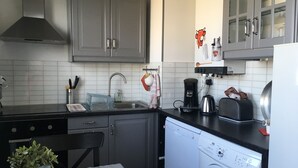 A compact kitchen with grey cabinets, a stainless steel sink, a coffee maker, a toaster, and a washing machine. - F2 modern and functional with sea view jet countryside Beach juno beach (Courseulles-sur-Mer)
