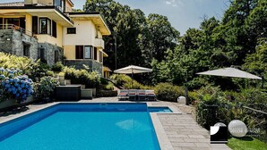 Ein modernes, zweistöckiges Haus mit Swimmingpool, Sitzgelegenheiten im Freien und üppiger Bepflanzung.