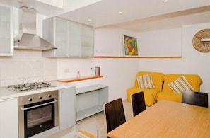 Modern kitchen with gas stove and oven, adjacent dining area with wooden table and sofa.