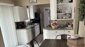 A modern kitchen with white cabinets, a black refrigerator, and a dining area with a wooden table and chairs. -  Come,Stay a While-WYNN Hosp.,Nexus Center,Cooperstown,Utica,Herkimer, Old Forge (Clayville)