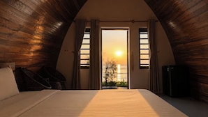 A room with a bed, a chair, a table, and a view of the sunset through a window. - Hoa Loi Resort (Xuan Canh)