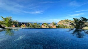 A clear blue infinity pool with a view of the ocean and palm trees. - Hoa Loi Resort (Xuan Canh)