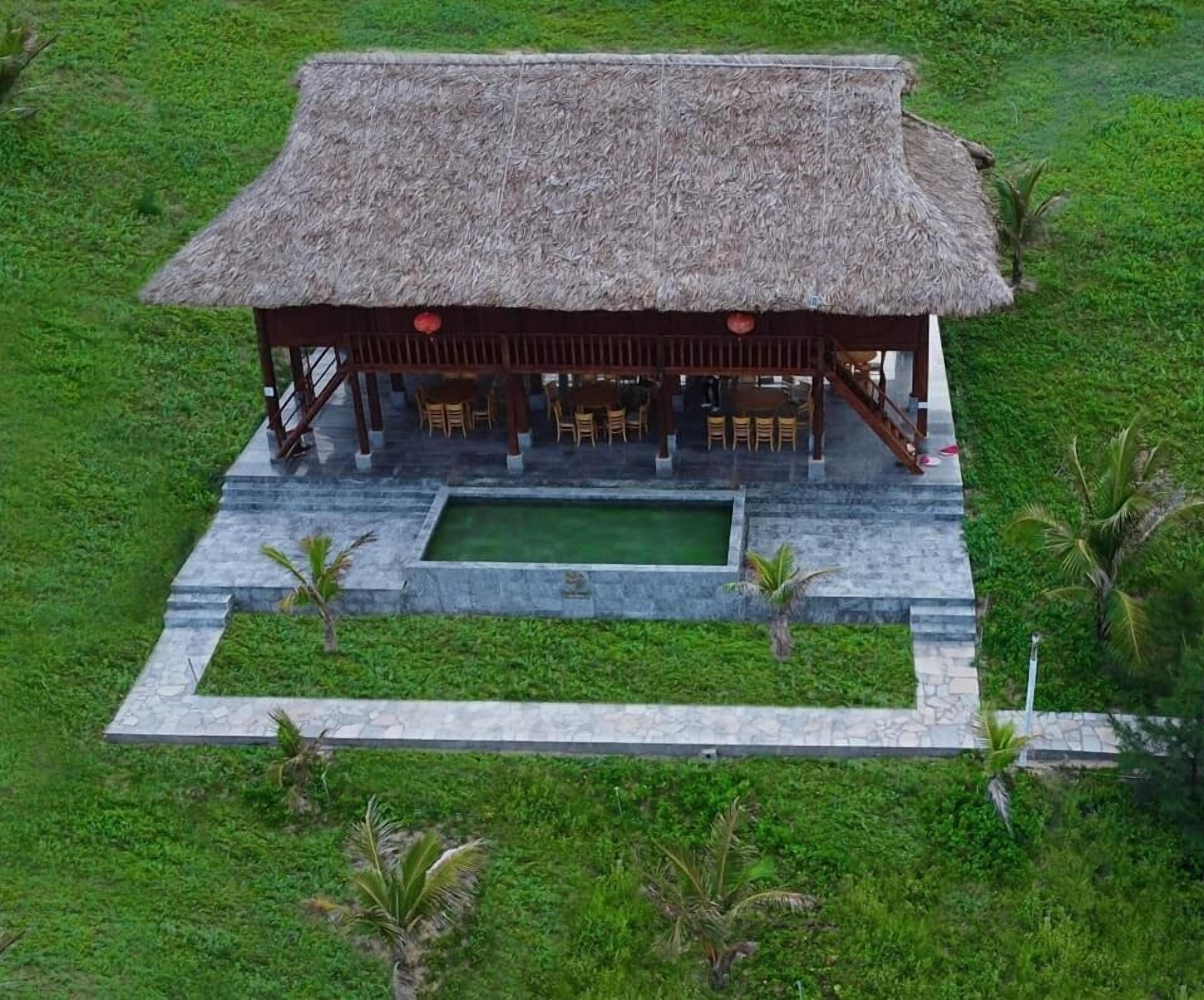 A thatched-roof structure with outdoor seating and a rectangular pool.