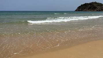A beach with clear water, a sandy shore, and a rocky outcrop in the distance.