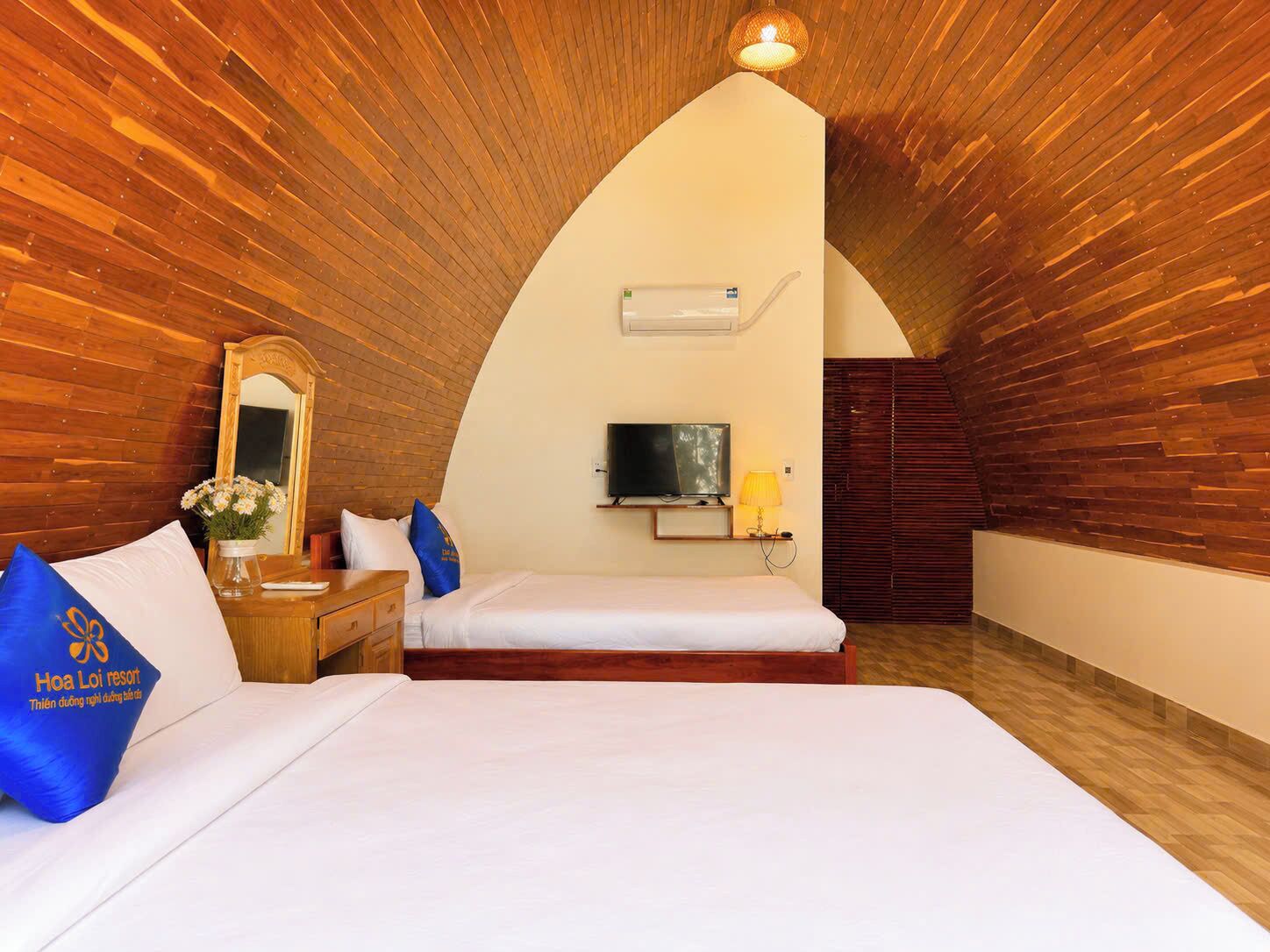 An arched room with wooden walls, a bed, a TV, and a desk with a lamp.